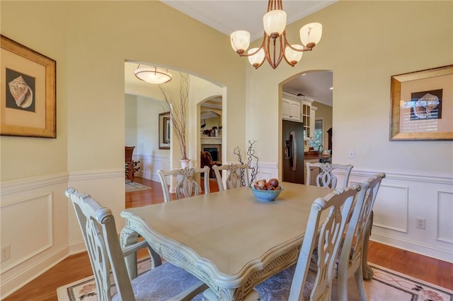 dining space with a wainscoted wall, wood finished floors, an inviting chandelier, a fireplace, and a decorative wall