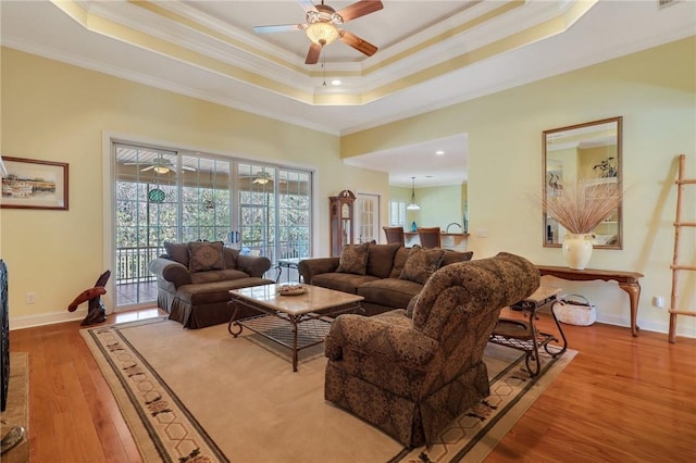 living area featuring crown molding, baseboards, a raised ceiling, and wood finished floors