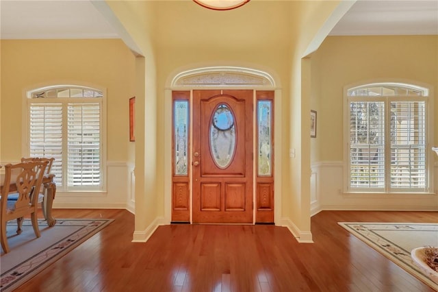 foyer with wood-type flooring, a healthy amount of sunlight, and wainscoting