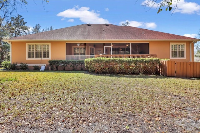 rear view of house with stucco siding, fence, a sunroom, and a yard