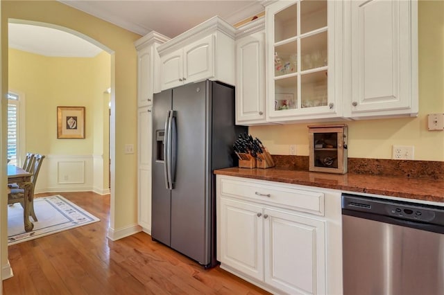 kitchen with light wood finished floors, arched walkways, white cabinets, glass insert cabinets, and appliances with stainless steel finishes