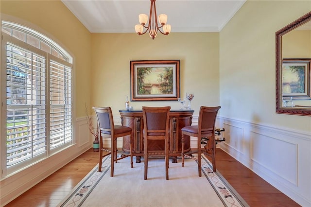 dining room with a wainscoted wall, light wood-style flooring, crown molding, a bar, and a notable chandelier