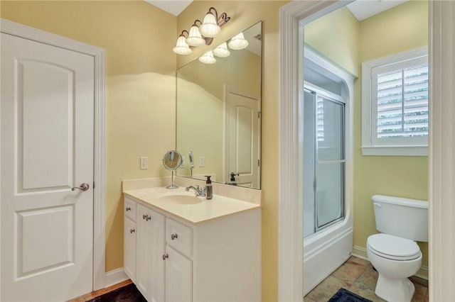 bathroom featuring toilet, combined bath / shower with glass door, vanity, and baseboards