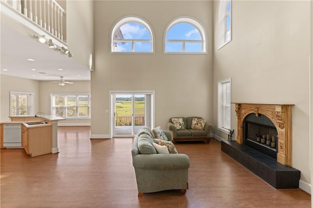 living room with a towering ceiling, hardwood / wood-style flooring, ceiling fan, and sink