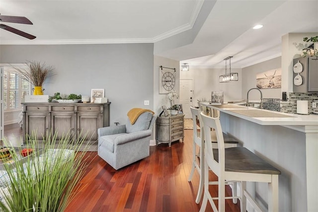 interior space featuring dark wood-style floors, pendant lighting, crown molding, light countertops, and a kitchen bar