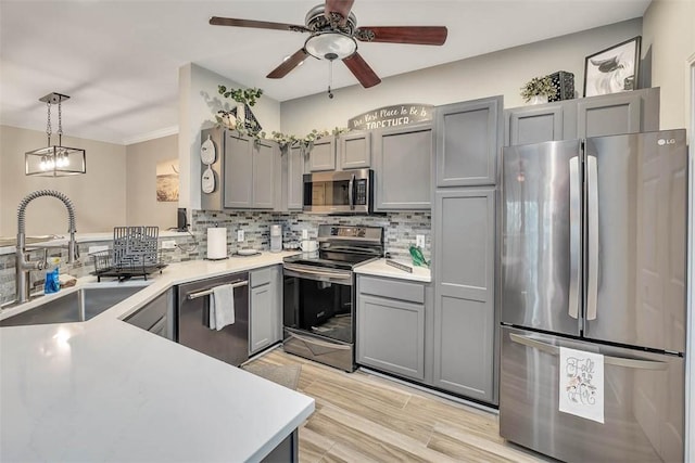 kitchen featuring appliances with stainless steel finishes, decorative light fixtures, light countertops, gray cabinetry, and a sink