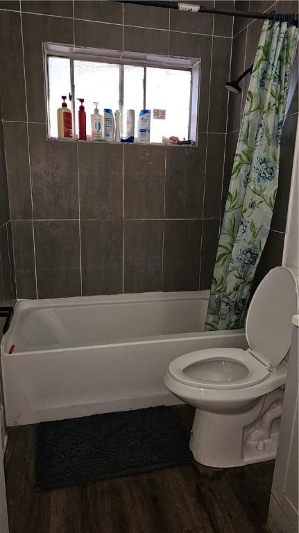 bathroom with a wealth of natural light, wood-type flooring, toilet, and shower / bath combo with shower curtain