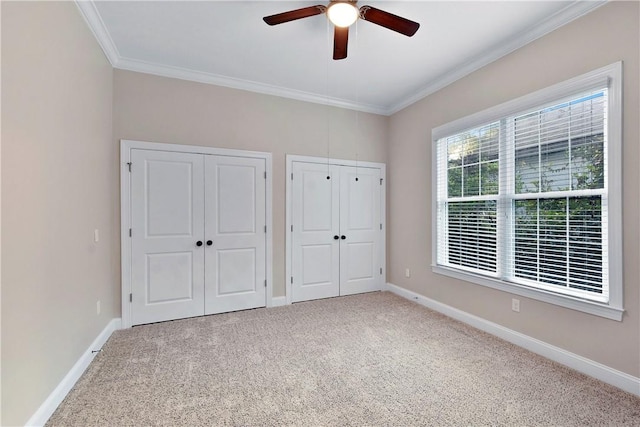 unfurnished bedroom with multiple closets, crown molding, carpet, and ceiling fan