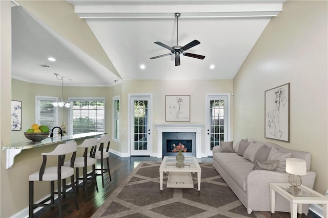 living room featuring ceiling fan with notable chandelier, dark hardwood / wood-style flooring, vaulted ceiling, and crown molding