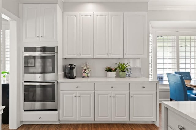 kitchen with stainless steel double oven, crown molding, white cabinets, light countertops, and wood finished floors