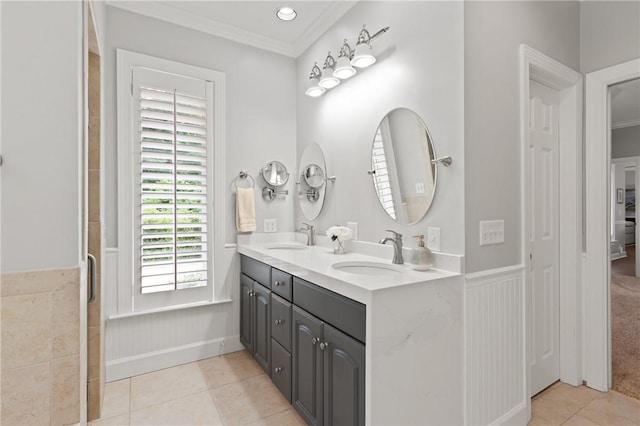 bathroom featuring tile patterned floors, crown molding, double vanity, wainscoting, and a shower with door