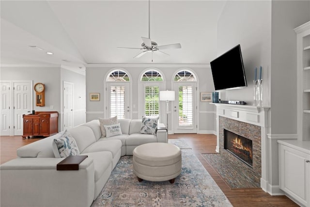living room with lofted ceiling, a ceiling fan, wood finished floors, a fireplace with flush hearth, and crown molding