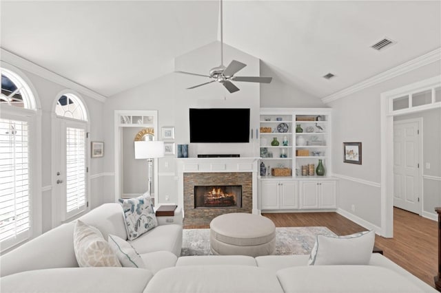 living area featuring ceiling fan, wood finished floors, a stone fireplace, lofted ceiling, and crown molding