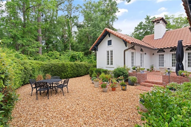 back of property featuring a chimney, stucco siding, a tile roof, a patio, and outdoor dining space
