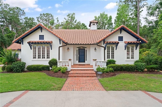 mediterranean / spanish-style home with a chimney, a front yard, and stucco siding
