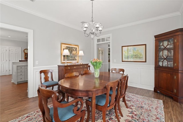 dining room featuring a chandelier, wood finished floors, a wainscoted wall, and crown molding