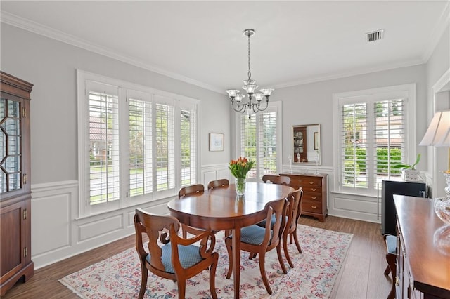 dining room with a chandelier, crown molding, wood finished floors, and a wainscoted wall