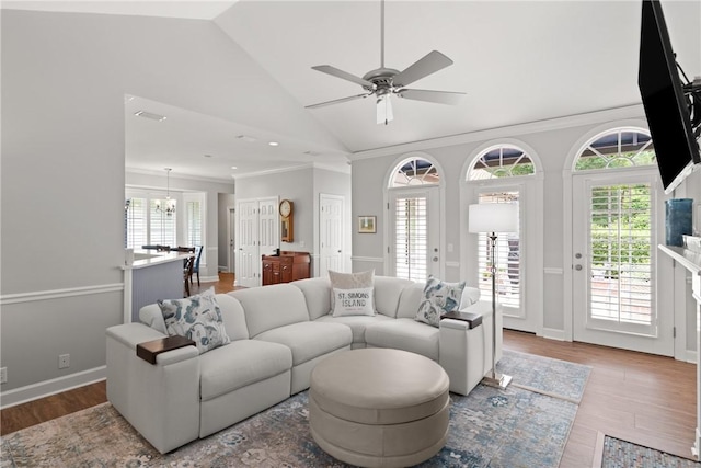 living area featuring a ceiling fan, wood finished floors, crown molding, high vaulted ceiling, and a chandelier