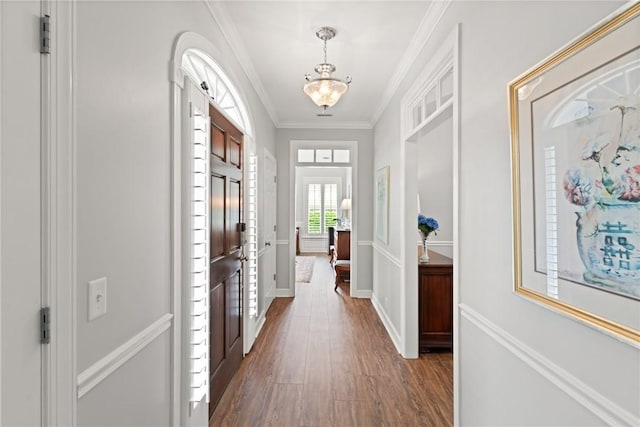 foyer entrance featuring wood finished floors, ornamental molding, baseboards, and a chandelier