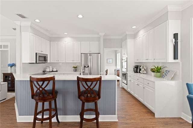 kitchen with appliances with stainless steel finishes, a breakfast bar, white cabinets, ornamental molding, and wood finished floors