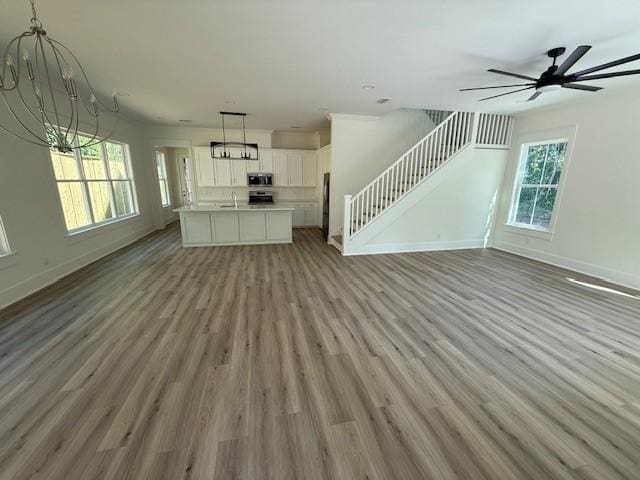 117 Quamley Wells Dr, Saint Simons Island, GA 31522 - unfurnished living room with a chandelier, stairs, light wood-style floors, and baseboards