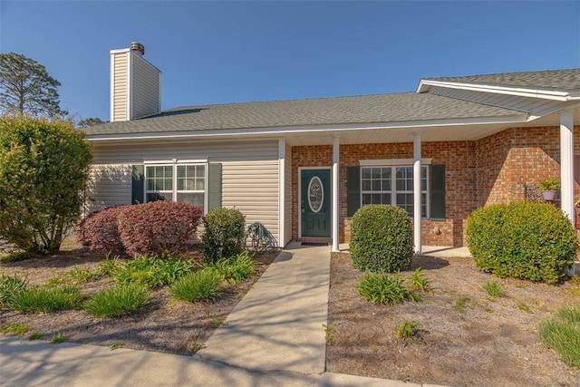 entrance to property featuring brick siding, roof with shingles, and a chimney