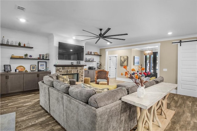 living room featuring ornamental molding, a barn door, dark hardwood / wood-style floors, and a brick fireplace