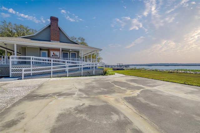 view of side of home featuring a water view, covered porch, and a lawn