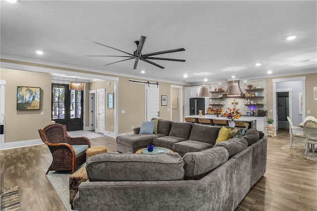 living room with wood-type flooring, ornamental molding, a barn door, and ceiling fan