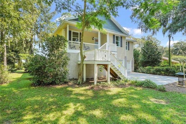 raised beach house featuring a front yard, covered porch, stairs, concrete driveway, and a garage