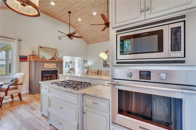 kitchen with light wood-type flooring, a tiled fireplace, open floor plan, appliances with stainless steel finishes, and wooden ceiling