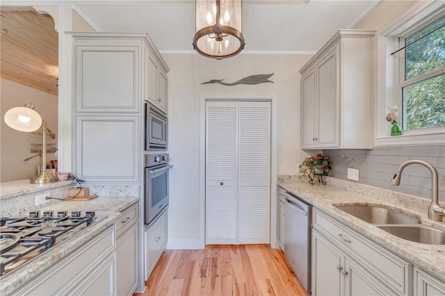 kitchen with light wood finished floors, a sink, stainless steel appliances, crown molding, and backsplash