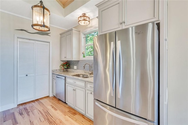 kitchen featuring crown molding, light stone countertops, light wood-style floors, stainless steel appliances, and a sink