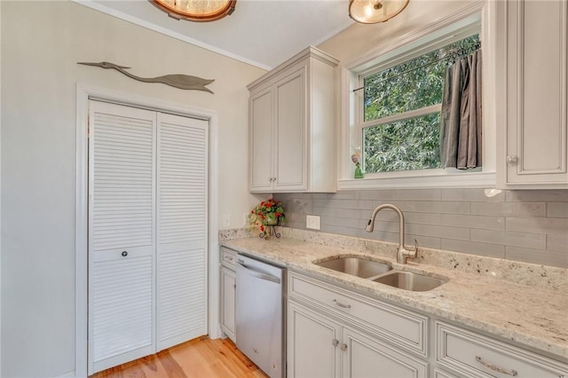 kitchen featuring backsplash, light stone countertops, stainless steel dishwasher, light wood-style floors, and a sink