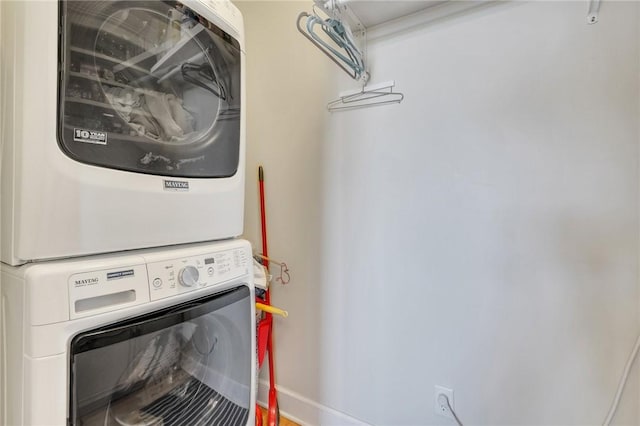 clothes washing area with stacked washer / dryer, laundry area, and baseboards