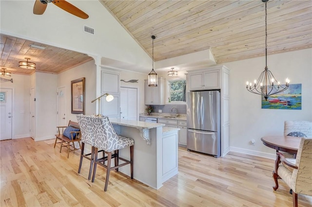 kitchen featuring a breakfast bar area, light stone countertops, visible vents, freestanding refrigerator, and wooden ceiling