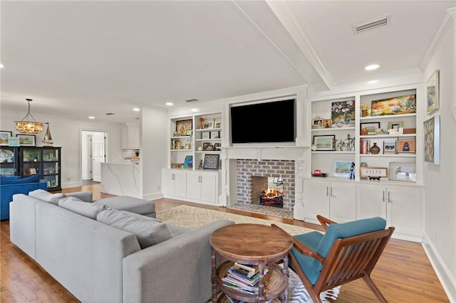 living room with a chandelier, ornamental molding, light wood-type flooring, a brick fireplace, and built in features