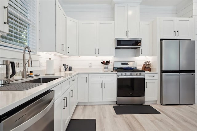 kitchen with sink, stainless steel appliances, ornamental molding, white cabinets, and light wood-type flooring