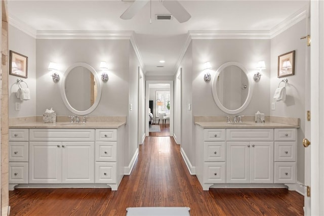 bathroom featuring ornamental molding, wood finished floors, and two vanities