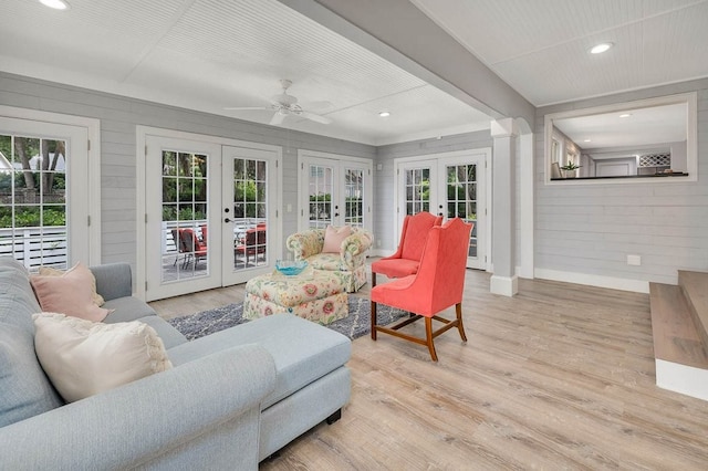 living room with french doors, light wood-type flooring, ceiling fan, and wood walls