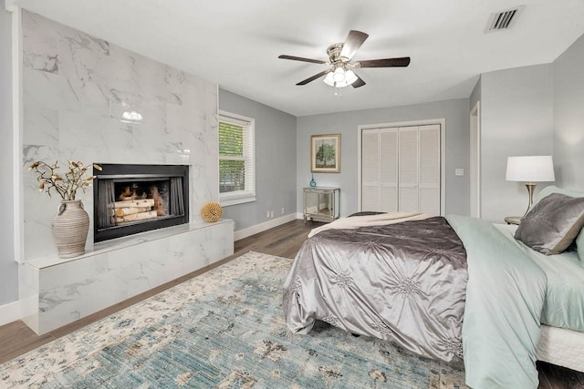 bedroom featuring a tile fireplace, dark hardwood / wood-style flooring, a closet, and ceiling fan