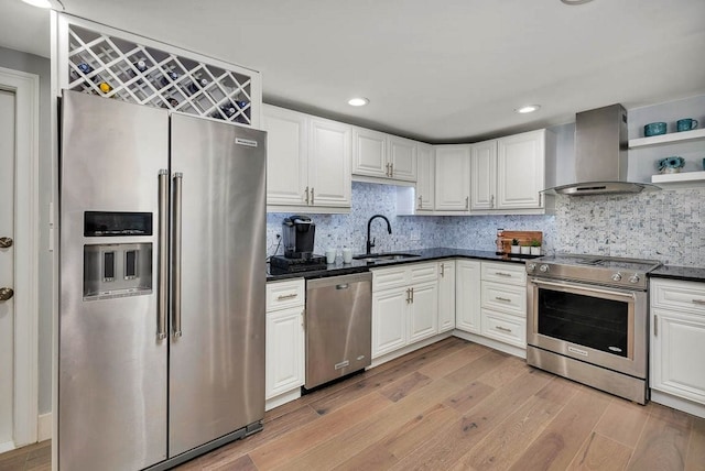 kitchen with backsplash, sink, wall chimney exhaust hood, light wood-type flooring, and stainless steel appliances