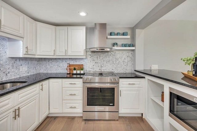 kitchen featuring light hardwood / wood-style floors, wall chimney range hood, stainless steel range with electric cooktop, and white cabinetry