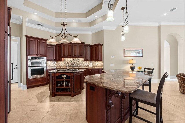 kitchen with stone counters, appliances with stainless steel finishes, pendant lighting, a kitchen breakfast bar, and a tray ceiling