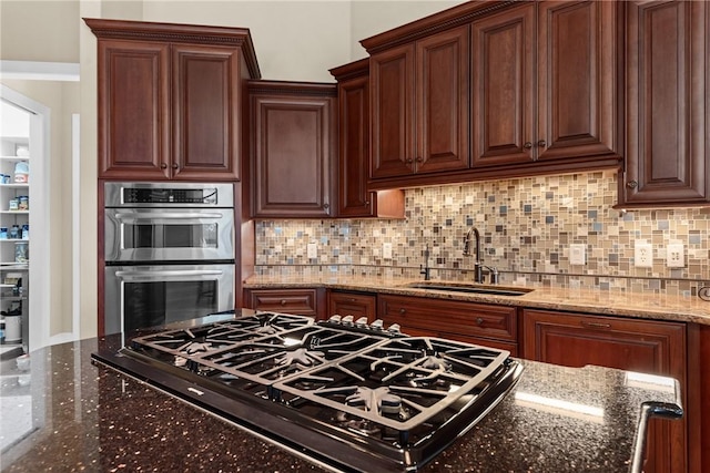 kitchen featuring double oven, sink, gas stovetop, and dark stone counters