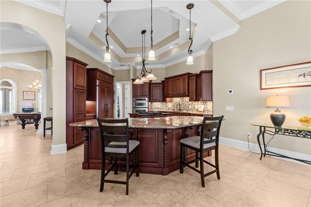 kitchen featuring a spacious island, a breakfast bar area, stone countertops, a tray ceiling, and pendant lighting