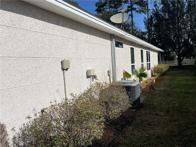 view of side of property with stucco siding, cooling unit, a yard, and fence