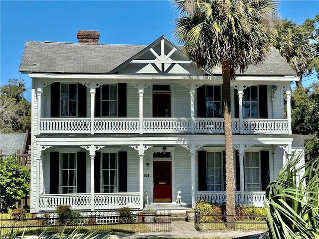 view of front of home with covered porch, a chimney, and a balcony