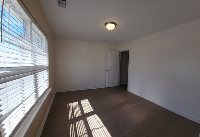 empty room featuring visible vents, baseboards, and dark wood-type flooring