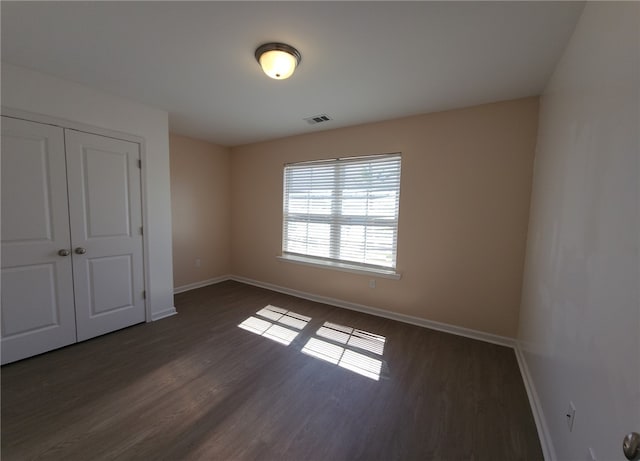 unfurnished bedroom featuring wood finished floors, visible vents, a closet, and baseboards